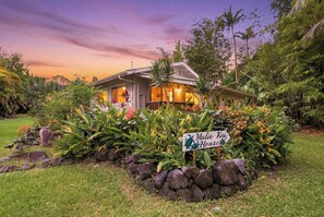 A house with a sign reading 'Malie Kai House' surrounded by tropical plants and a stone wall. - Malie Kai House at Island Rainforest Grove (Keaau)