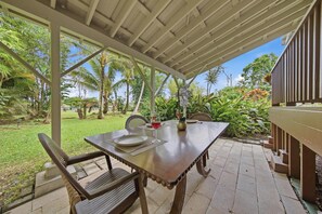 An outdoor patio with a table, chairs, and a covered area. - Malie Kai House at Island Rainforest Grove (Keaau)