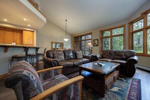 A spacious living room with a large L-shaped sectional sofa, a coffee table, and a patterned armchair. There are multiple windows providing natural light and views of the outdoors. - WS2748 | Winter Shuttle | Hot Tub | Pool | Gas Fireplace (Steamboat Springs)