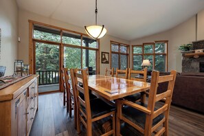 A wooden dining table with chairs, large windows, and a hanging light fixture in a room with a stone fireplace. - WS2748 | Winter Shuttle | Hot Tub | Pool | Gas Fireplace (Steamboat Springs)
