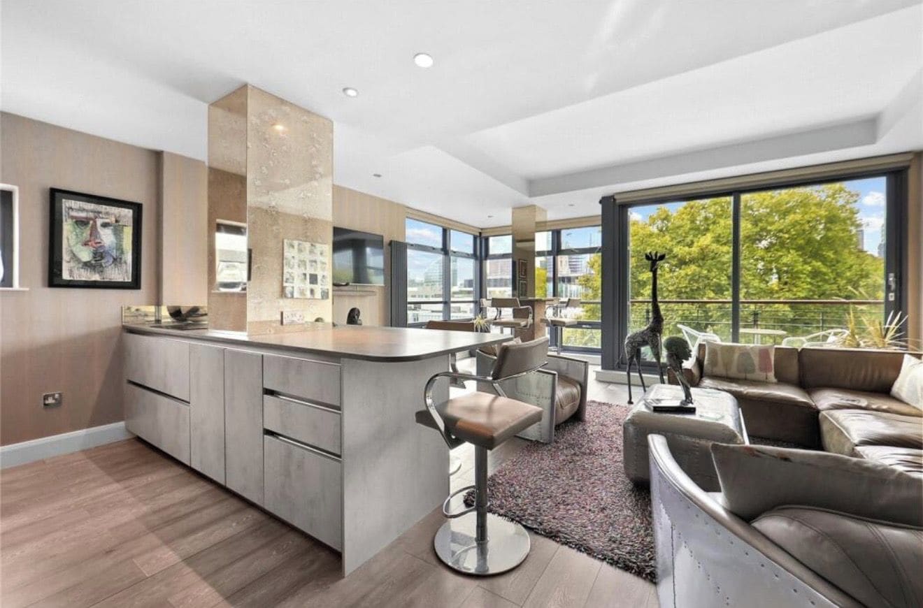 Een moderne keuken met een centraal eiland, barstoelen en een stadszicht door grote ramen.