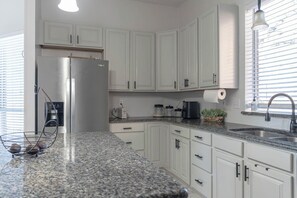 A kitchen with white cabinets, a stainless steel refrigerator, granite countertops, a coffee maker, and a window with blinds. - Spacious Arlington 5BR Sleeps 12 Near AT&T Stadium & Stovall Park (Arlington)
