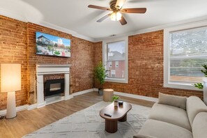 Ein Wohnzimmer mit Backsteinwand, Kamin, Deckenventilator und großem Fenster.