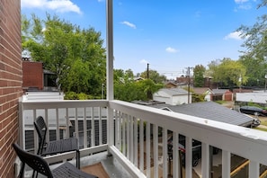 A balcony with a white railing, a black chair, and a table. - Historic Soulard 2BR | Stylish Balcony Retreat (St. Louis)