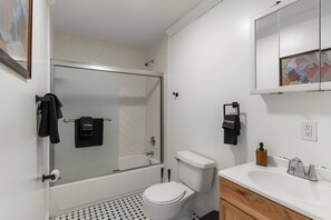 Moderni kylpyhuone, jossa on lasiseinällinen suihku, wc ja peilillä varustettu pesuallas.