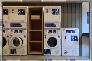 A laundry facility with four washing machines labeled 1 to 4, and a wooden shelf unit in the center. - Studio Nex One Faria Lima - A 3 min do Metrô (São Paulo)