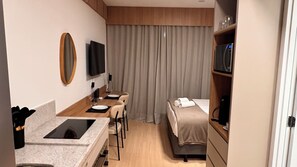 A hotel room with a kitchenette, a bed, a TV, and a large window with curtains. - Studio Nex One Faria Lima - A 3 min do Metrô (São Paulo)