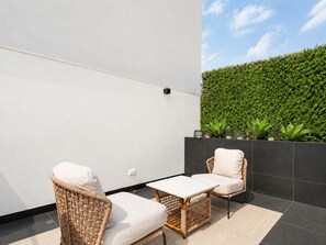A balcony with two wicker chairs, a small table, and a green hedge wall. - Suite de Diseño con Piscina y Rooftop  (San Isidro)