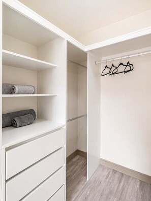 A walk-in closet with open shelves, a hanging rod, and a wooden floor. - Suite de Diseño con Piscina y Rooftop  (San Isidro)