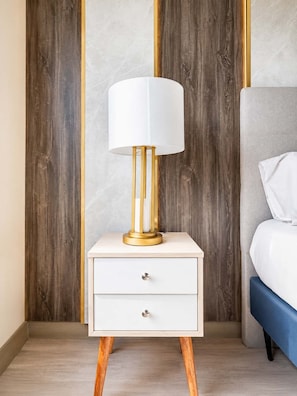 A bedside table with a lamp, a drawer, and a bed with a blue cover. - Suite de Diseño con Piscina y Rooftop  (San Isidro)