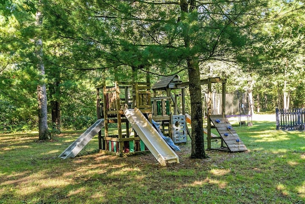 A playground with slides and climbing structures surrounded by trees.