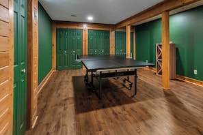 A room with a ping pong table, wooden flooring, green walls, and wooden doors.