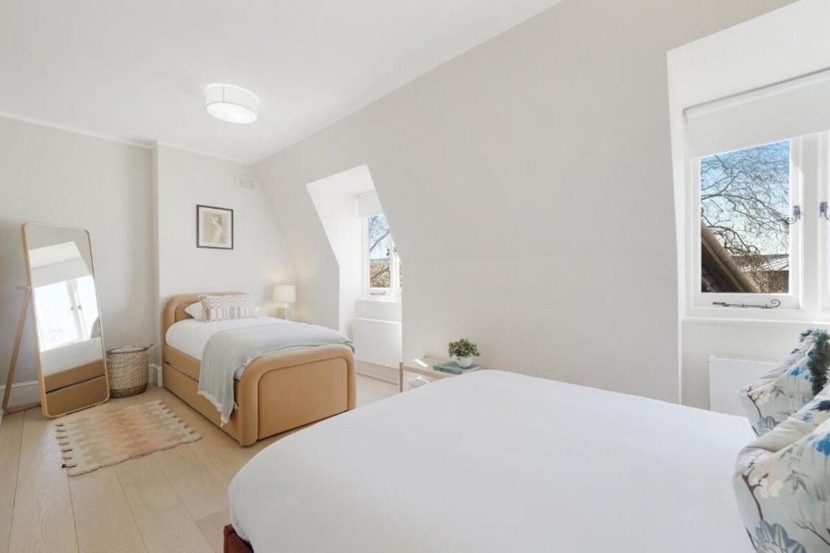 Ein Schlafzimmer mit einem Bett, einem Nachttisch, einem Spiegel und einem Fenster.