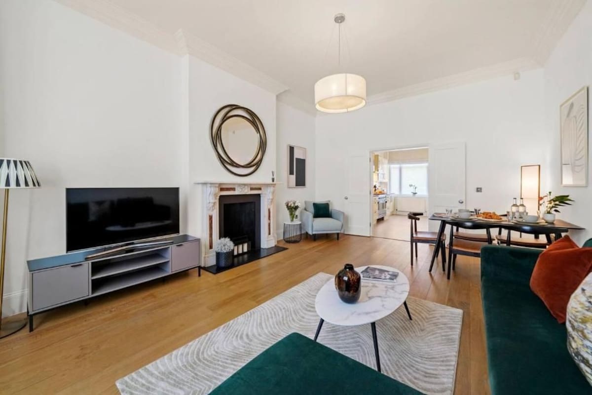 Ein modernes Wohnzimmer mit Flachbildfernseher, Kamin, Essbereich mit Tisch und Stühlen sowie einer Küche im Hintergrund.