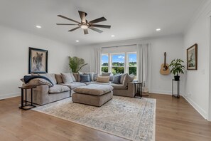 Ein Wohnzimmer mit einer Eckcouch, einem Deckenventilator und einem großen Fenster mit Blick.