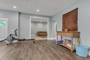 A room with a stationary bike, a sofa, a wooden console table, and a blue bucket. - Magical Family Escape: Treehouse, Games, Memories (Spring Hill)