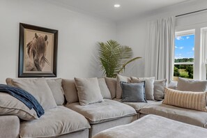 Ein Wohnzimmer mit einer Sofagarnitur, einem gerahmten Bild an der Wand, einer Topfpflanze und einem Fenster mit Blick.