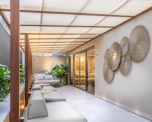 A modern outdoor seating area with a pergola, cushioned sofas, and decorative wall art. - Way Bossa #G2 - Flat in Bessa by Carpediem (João Pessoa)
