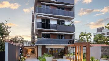 A multi-story residential building with balconies, a covered walkway, and a garden area.