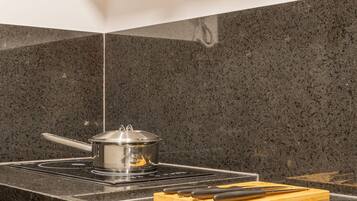 A kitchen with a black granite countertop, a stove, a pot, and a cutting board.