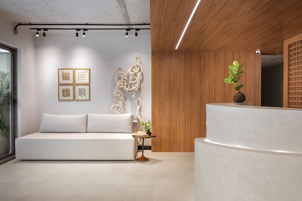 A modern interior with a white sofa, framed artwork, a small table with a plant, and a wooden wall. - Way Bossa #G2 - Flat in Bessa by Carpediem (João Pessoa)