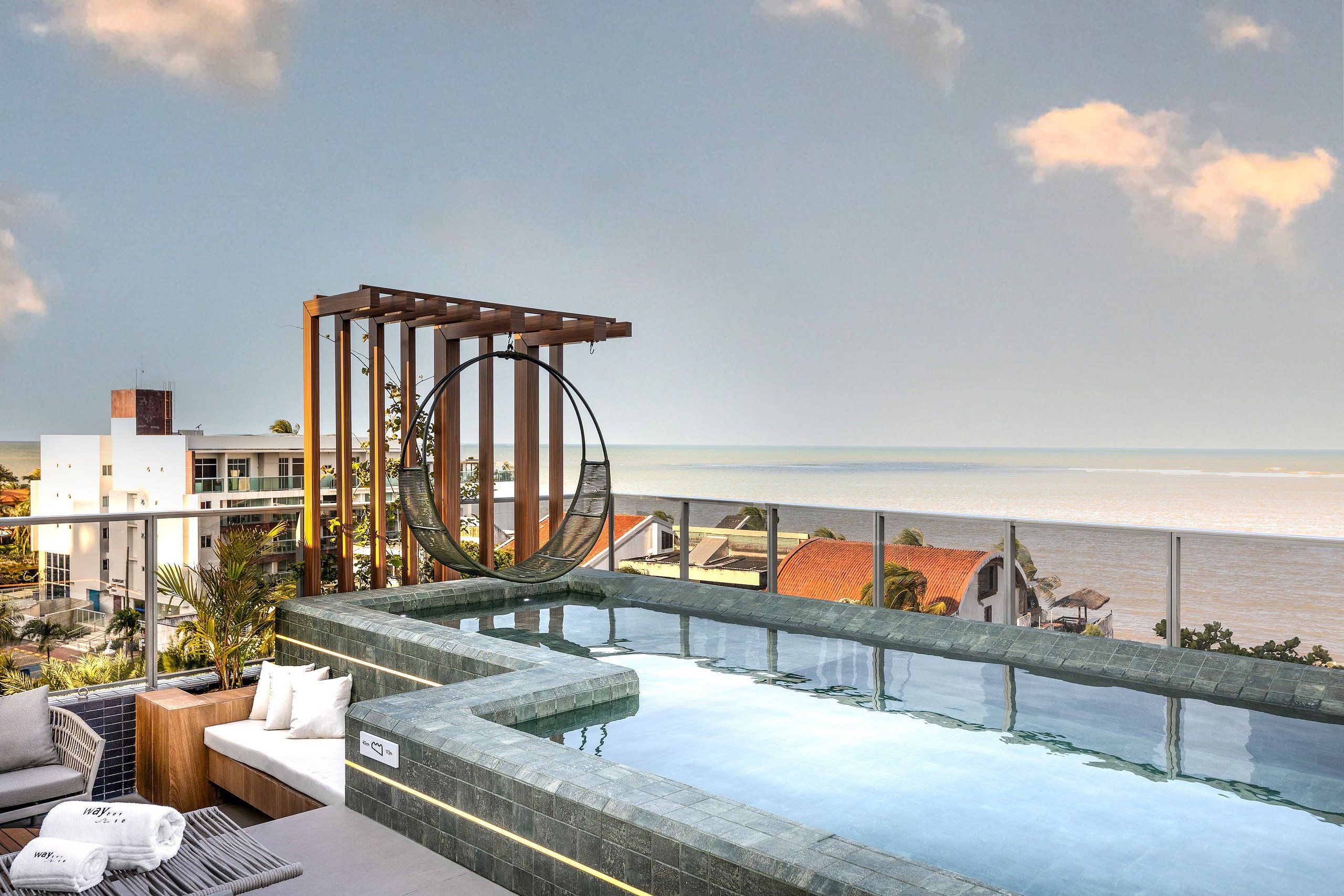 A rooftop infinity pool with a hammock, lounge chairs, and a view of the ocean.