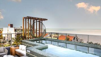 A rooftop infinity pool with a hammock, lounge chairs, and a view of the ocean.
