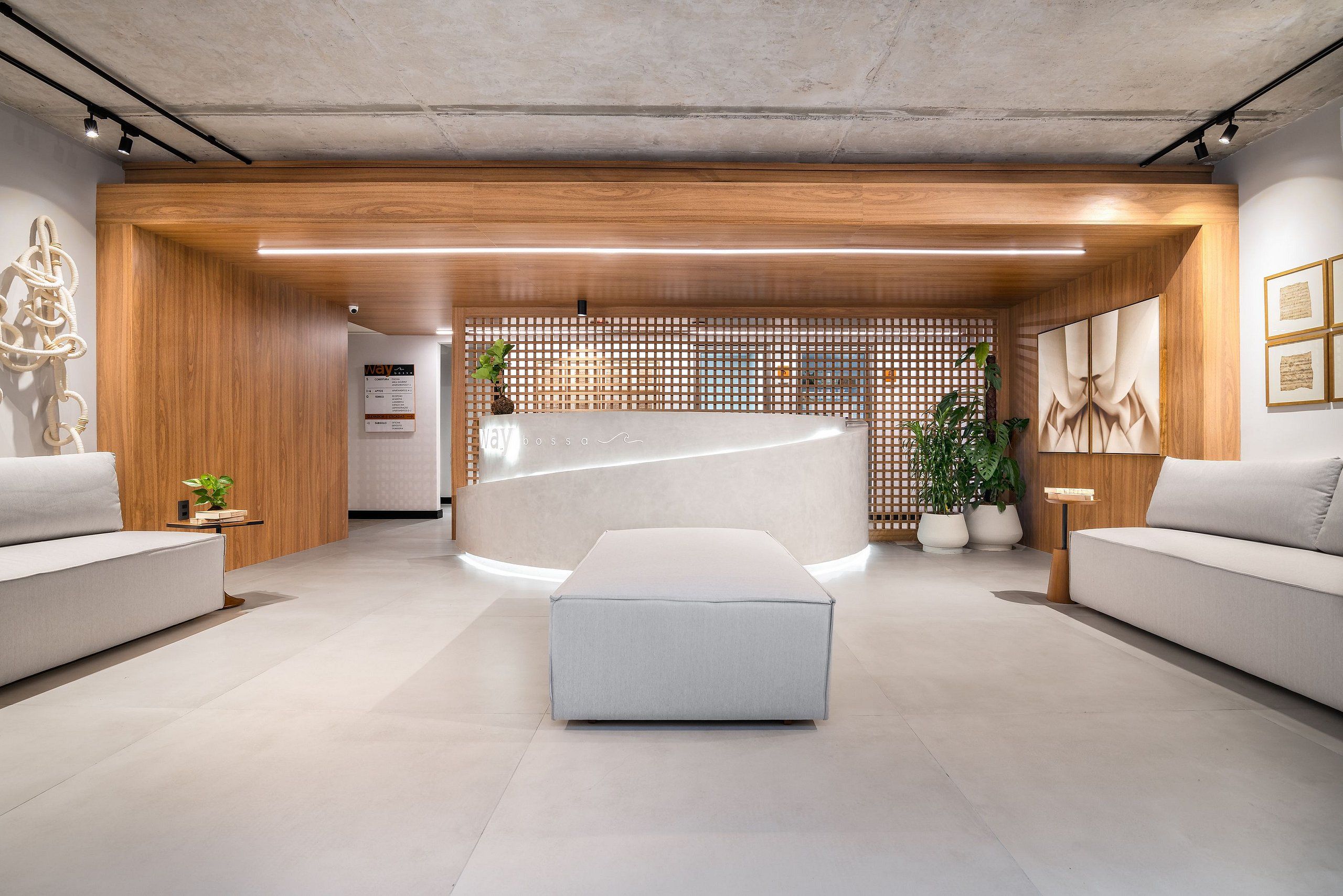 A modern reception area with a reception desk, two sofas, a large ottoman, wooden paneling, and a plant.