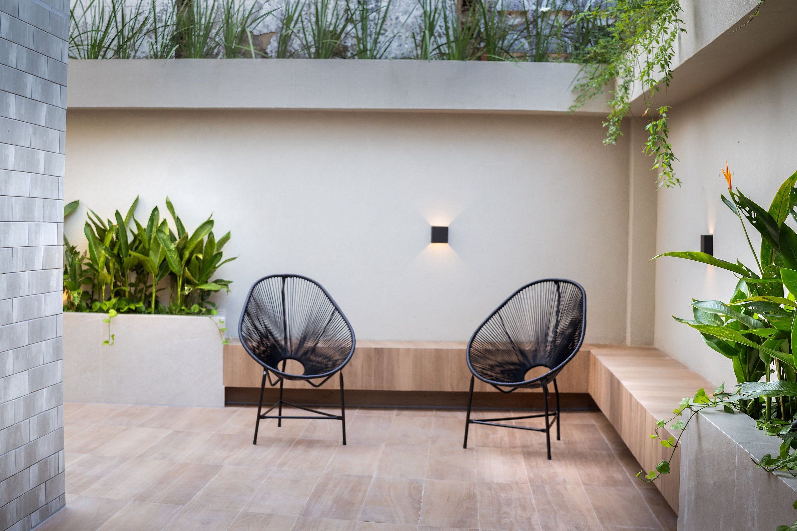Un área de estar moderna al aire libre con dos sillas, una lámpara y plantas.