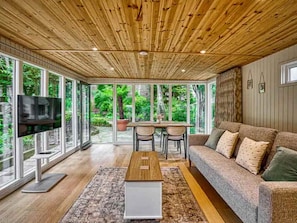 A room with a wooden ceiling, a television, a sofa, a table, and large windows. - Garden Studio in Victoria Park - Free Parking (Manchester)