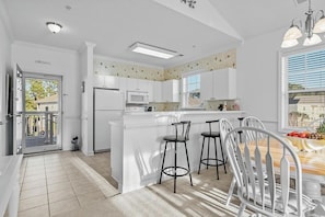 A kitchen with white cabinets, a microwave, and a dining area with a wooden table and bar stools. - Barefoot Willowbend 231 Free Shuttle to Pool/Beach (North Myrtle Beach)