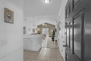 A hallway leading to a kitchen with white cabinetry, a chandelier, and a Christmas tree. - Barefoot Willowbend 231 Free Shuttle to Pool/Beach (North Myrtle Beach)