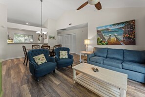 A living room with a blue sofa, two armchairs, a coffee table, and a painting of a coastal scene. - W Hyde Pk 11E in Kingston 2nd floor, Pool, Beach (Myrtle Beach)