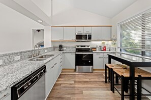 Et moderne køkken med granitbordplader, rustfrie stålapparater og et træspisebord.