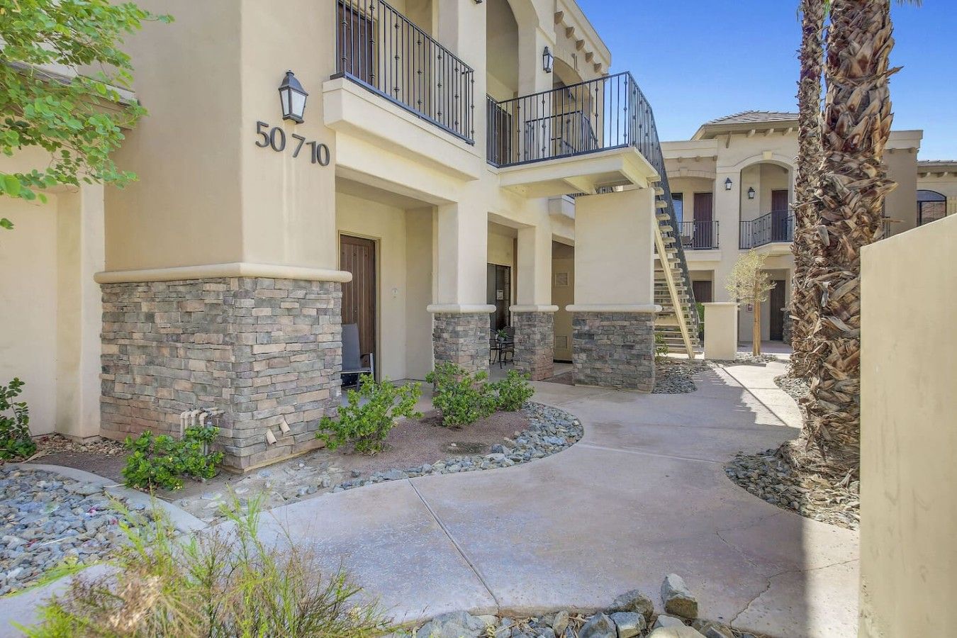 A multi-story residential building with stone accents, a visible balcony, and a clear sky.