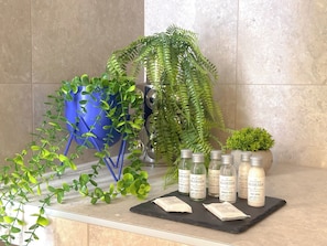 Ein Badezimmer-Waschtisch mit einer Topfpflanze, einer blauen Vase und mehreren Flaschen mit Aloe Vera Produkten.