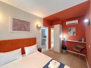 Ein Hotelzimmer mit Bett, Schreibtisch, Stuhl, Klimaanlage und Wandgemälde.