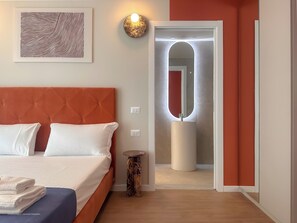 Ein Schlafzimmer mit einem Bett, einem Nachttisch, einer Wandleuchte und einer Tür zu einem anderen Raum.