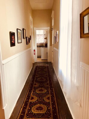 A hallway with a patterned carpet, white wainscoting, and framed pictures on the walls. - Victorian 2 bedroom sleeps six by Forsyth Park (Savannah)