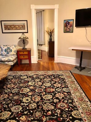 Une pièce avec un tapis à motifs, un canapé, une petite table et un téléviseur.