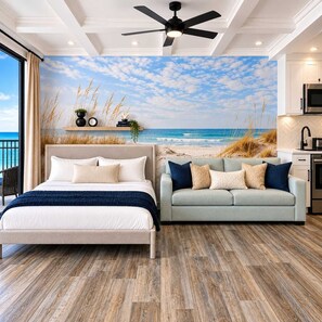A bedroom with a bed, a sofa, a ceiling fan, and a view of the beach through a mural. - Beachfront Studio Retreat with Resort Amenities at Yachtsman S1104 (Myrtle Beach)