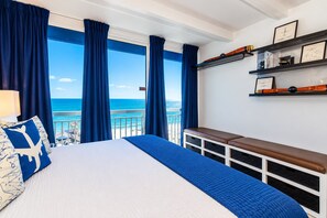 A hotel room with a large bed, a view of the ocean, a balcony with a railing, and a shelf with framed items. - Fly Away to Your Myrtle Beach Getaway! Landing at Yachtsman S1105 Studio (Myrtle Beach)