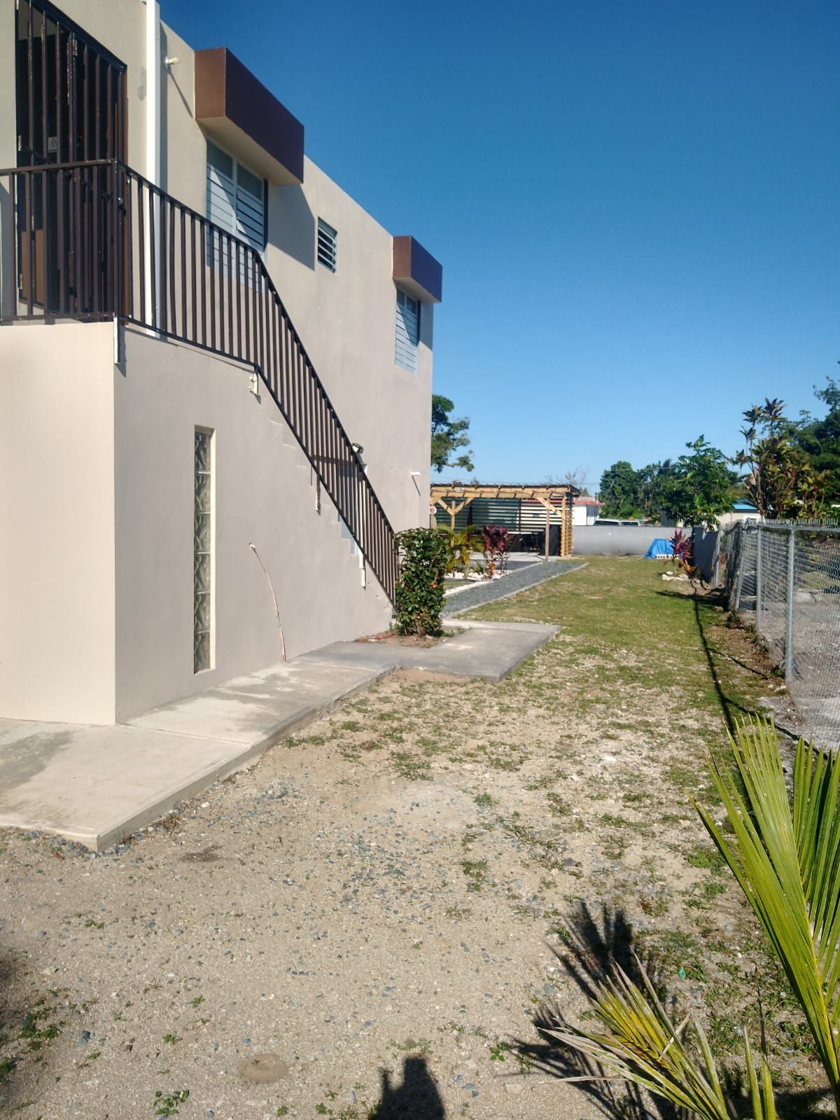 A residential building with a concrete staircase, a small garden area with sparse vegetation, and a clear blue sky.