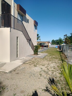 A residential building with a concrete staircase, a small garden area with sparse vegetation, and a clear blue sky.