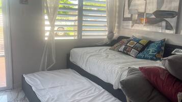 A bedroom with a bed, a window with curtains, a wall art piece, and a tiled floor.