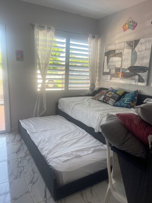 A bedroom with a bed, a window with curtains, a wall art piece, and a tiled floor.