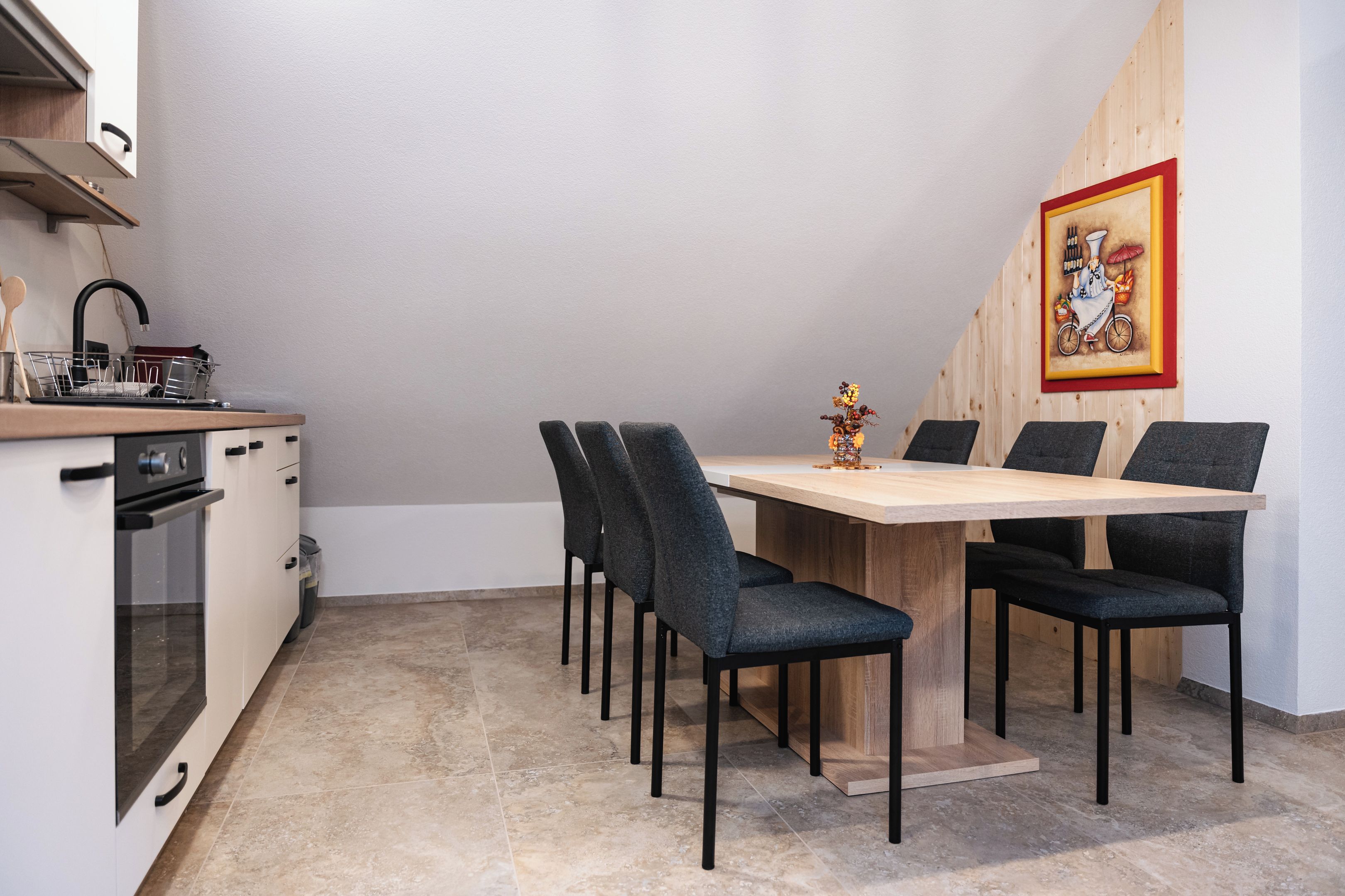 Een compacte keuken met een eethoek, met een houten tafel en stoelen, een klein spoelgedeelte en een fornuis.