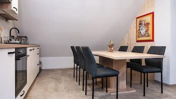 Een compacte keuken met een eethoek, met een houten tafel en stoelen, een klein spoelgedeelte en een fornuis.