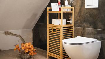 Een moderne badkamer met een houten plank met toiletartikelen, een toilet en een decoratieve mand met herfstbladeren.