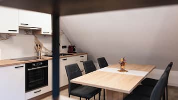Een moderne keuken met een inbouwoven, een magnetron en een koffieapparaat. Er staat een eettafel met zes stoelen bij, en een vaas met bloemen erop.